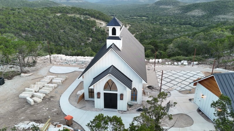 Aerial view of The Chapel at Wimberley, a white steepled wedding chapel on a Texas Hill Country hilltop surrounded by miles of green cedar and oak