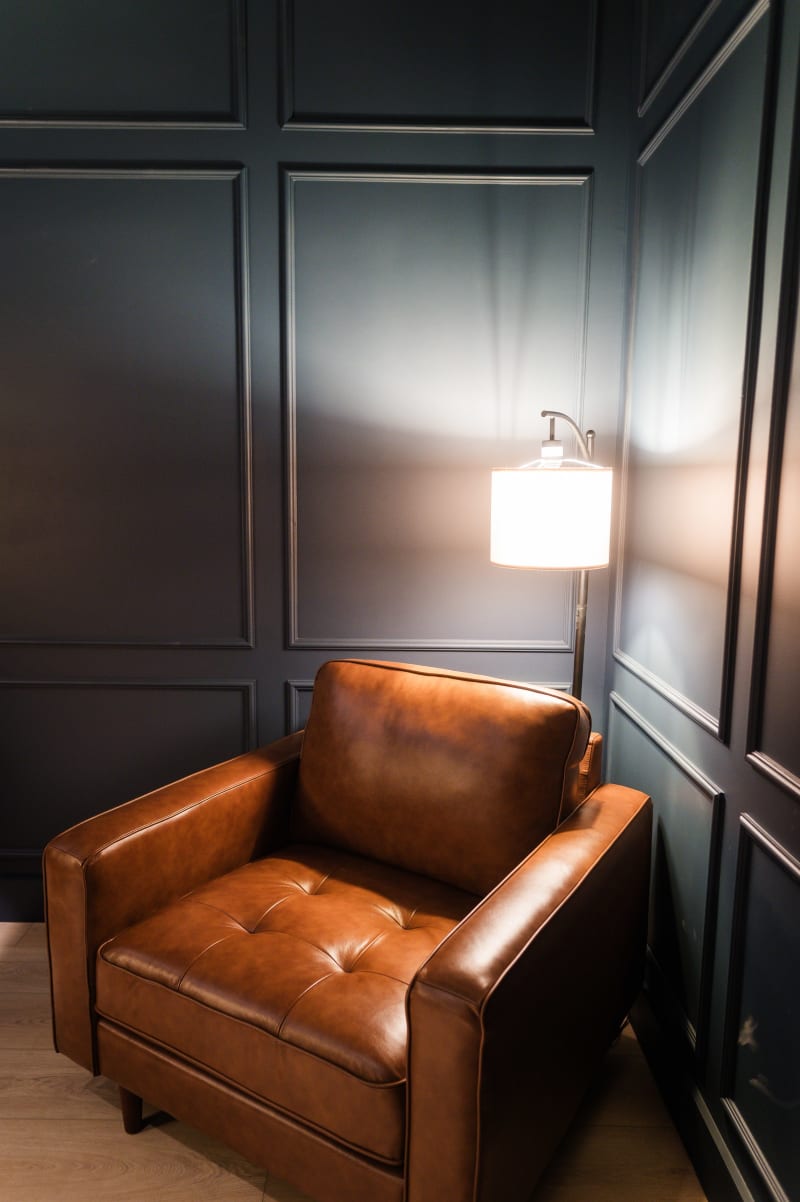Groom's lounge at The Chapel at Wimberley with dark paneled walls, a cognac leather armchair, and a floor lamp