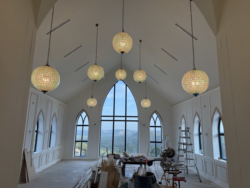 Sanctuary of The Chapel at Wimberley with crystal orb chandeliers hanging from the vaulted ceiling and a great arched window framing the Hill Country